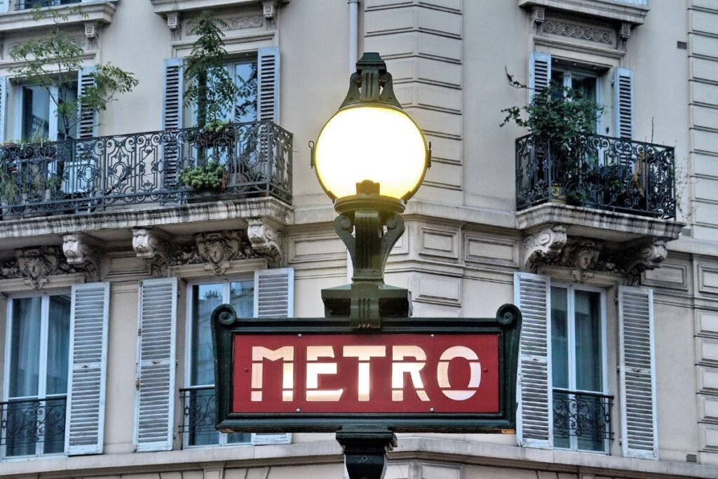 A bustling Parisian metro station, Ligne 1 and 4 intersection, captured in a dynamic wide-angle view. The platform is filled with commuters hurrying to their destinations, their figures in motion blurred to suggest the pace of urban life. Warm, diffused lighting filters in from above, casting a soft glow on the sleek, tiled walls and metal benches. The scene evokes a sense of efficiency and convenience, reflecting the "well-located, affordable" theme of the article's section. The perspective draws the viewer into the heart of this transportation hub, conveying the ease of navigating the city's public transit network. Entrada de Uma Estação do Metrô de Paris