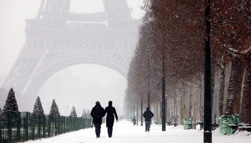 A scenic view of Paris in the off-season, with a charming, uncrowded city center under a soft, overcast sky. In the foreground, a couple strolling along a quaint, cobblestone street, free to explore at their own pace without the usual throngs of tourists. In the middle ground, the iconic Notre-Dame Cathedral stands majestically, its gothic spires rising against a muted palette of grays and blues. In the background, the Seine River winds through the cityscape, its calm waters reflecting the subtle beauty of the season. The atmosphere is one of tranquility and contemplation, inviting the viewer to savor the city's timeless allure without the typical crowds and bustle. O Inverno em Paris pode ser bastante frio