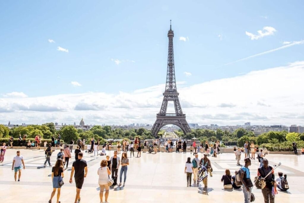 A picturesque Parisian street scene, with the iconic Eiffel Tower visible in the distance. In the foreground, a group of tourists are consulting a map, their faces alight with excitement. The middle ground features charming sidewalk cafes, their striped awnings casting warm shadows across the cobblestones. Passersby stroll leisurely, taking in the sights and sounds of this vibrant city. Warm, golden lighting illuminates the scene, creating a sense of timeless wonder. The overall atmosphere evokes the essence of Paris - a harmonious blend of history, culture, and joie de vivre. Melhor época para visitar os Pontos Turísticos de Paris