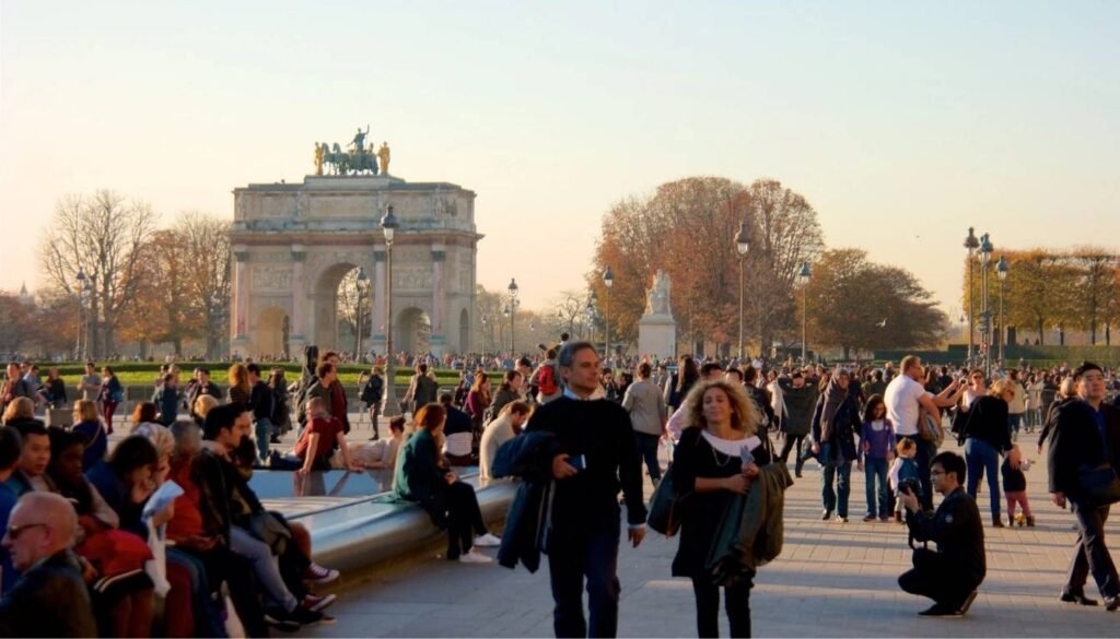 A vibrant Parisian street scene in the evening, showcasing the elegant and refined etiquette of the locals. In the foreground, well-dressed Parisians stroll along the sidewalk, exuding an air of sophistication and poise. Soft, warm lighting from nearby cafes and boutiques casts a cozy glow, highlighting the intricate details of their attire - tailored suits, silk scarves, and polished leather shoes. In the middle ground, couples dine at outdoor tables, engaged in lively conversation while sipping on glasses of fine wine. The background features the iconic Parisian architecture, with ornate facades and wrought-iron balconies. An atmosphere of refined leisure and cultural appreciation pervades the scene, reflecting the essence of Parisian etiquette. A etiqueta é importante em Paris - Paris sem falar francês