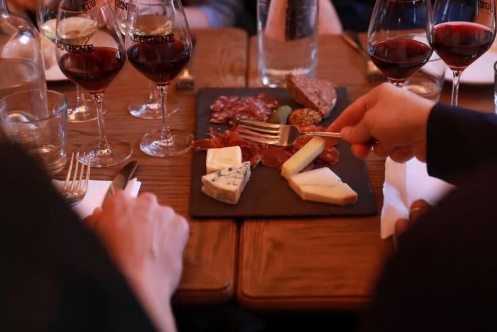 A cozy French bistro interior, with a wooden table set with an array of artisanal cheeses and a selection of fine wines. Soft, warm lighting creates a inviting atmosphere, while the background features exposed brick walls and vintage decor. In the foreground, a cheese board showcases various textures and flavors, accompanied by a carafe of deep red wine and elegant glassware. The overall scene evokes the quintessential Parisian dining experience, capturing the essence of indulgence and culinary sophistication. Queijos e Vinhos estão entre as principais comidas típicas de Paris